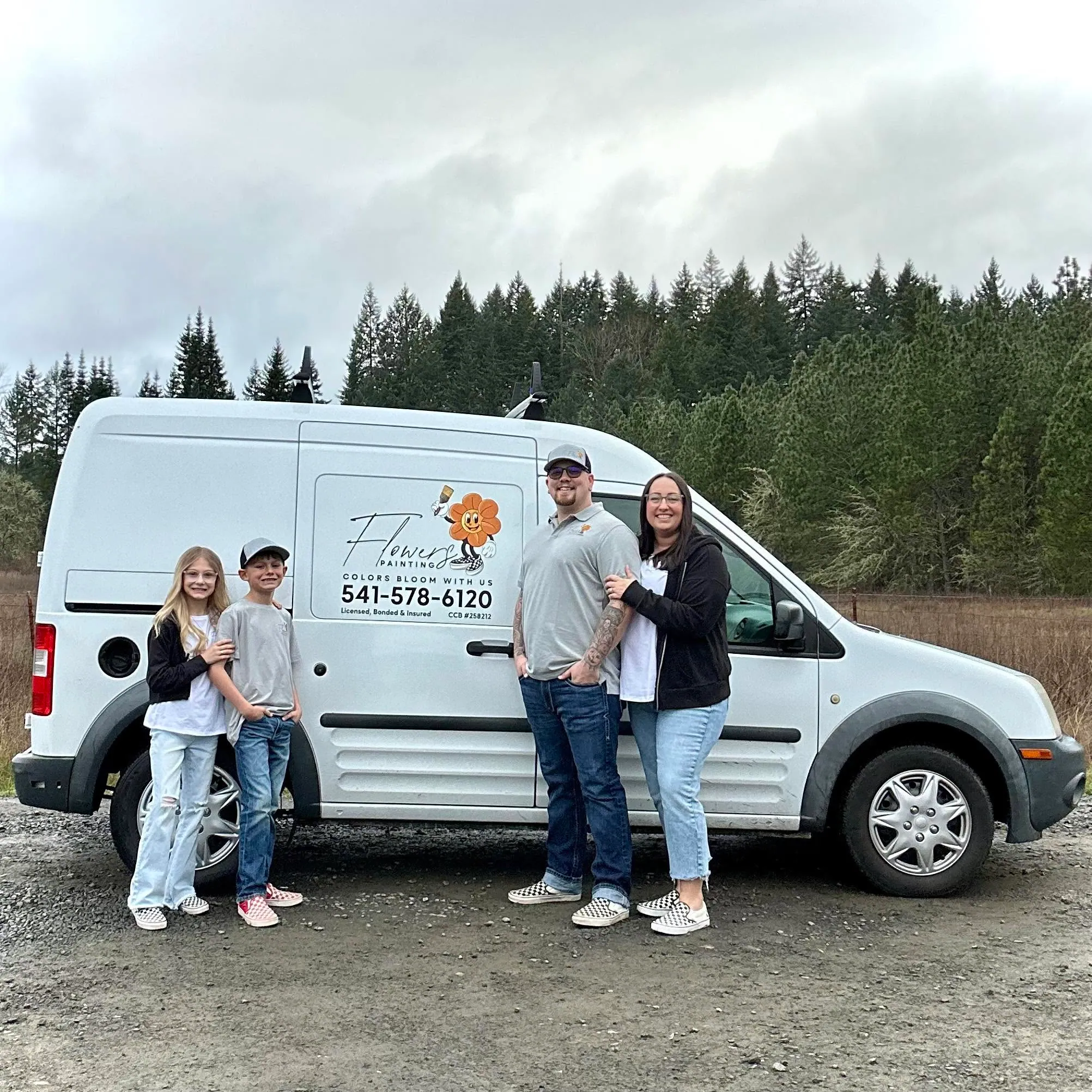 A family of four beside their lettered Flowers Painting work van, fir trees behind