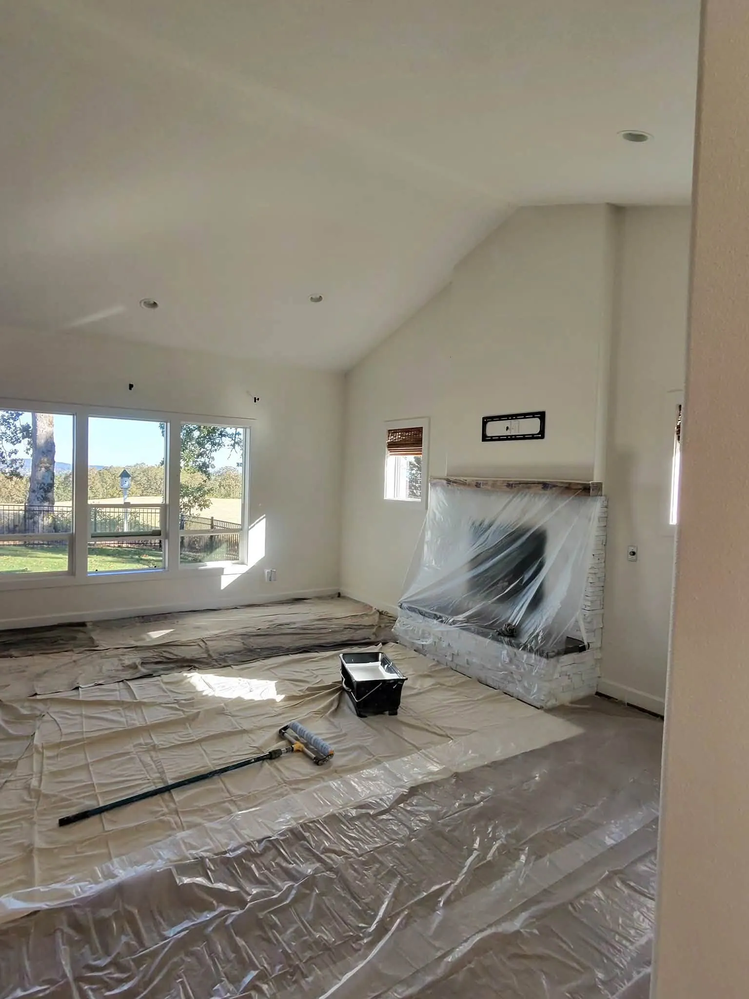 Living room ready for paint: floor sheeted in plastic, fireplace wrapped, roller and tray waiting